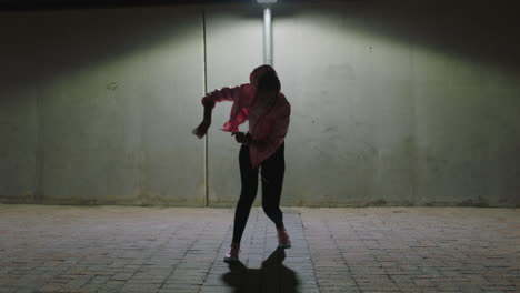 Mujer-Bailando-Joven-Bailarina-Callejera-Practicando-Movimientos-De-Baile-Modernos-De-Estilo-Libre-Bajo-La-Luz-De-La-Calle-En-La-Ciudad-Por-La-Noche