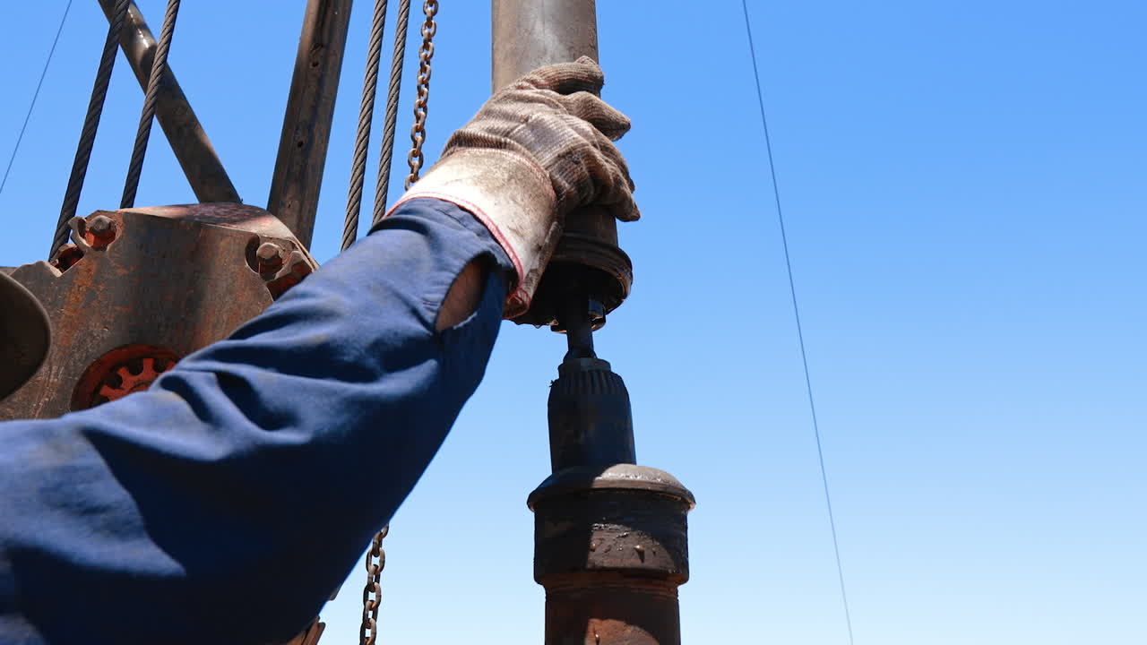 Man in helmet and glasses pulling the pipe down setting the equipment at oil production. Workers arrange the drilling machinery.