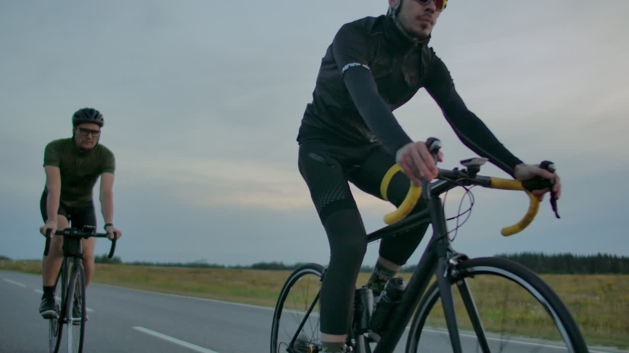 Handsome bearded professional male cyclist riding his racing bicycle in the morning together with his girlfriend both wearing protective helmets and eyeglasses sun shining through between them