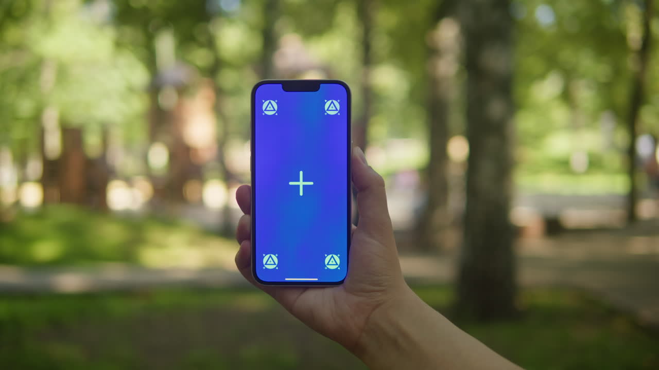 Young woman holding phone chroma key screen in the park close-up. Girl with green screen on smart phone. Nature