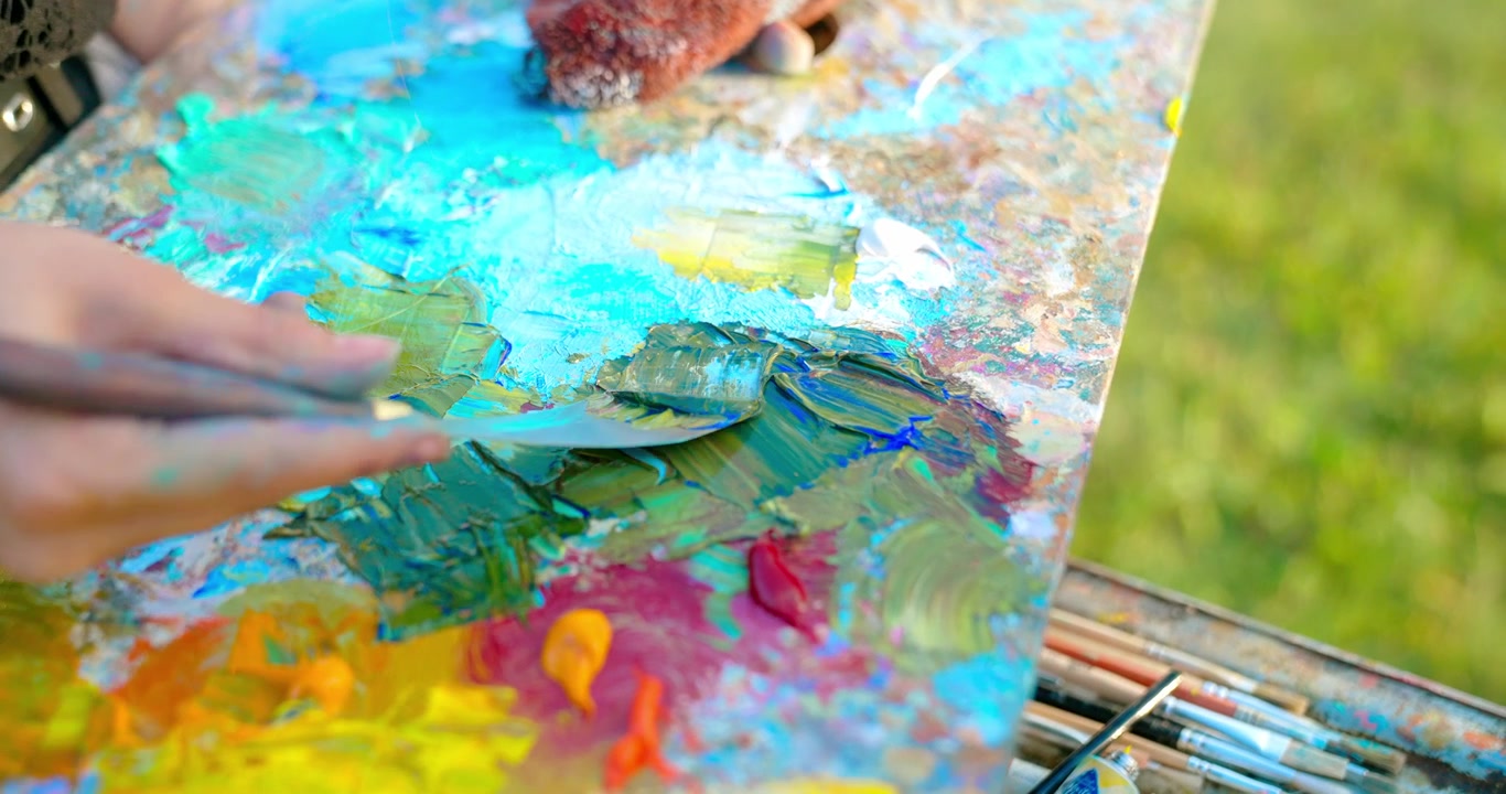 Primo piano di un artista che mescola vivaci colori a olio su una tavolozza con una spatola.