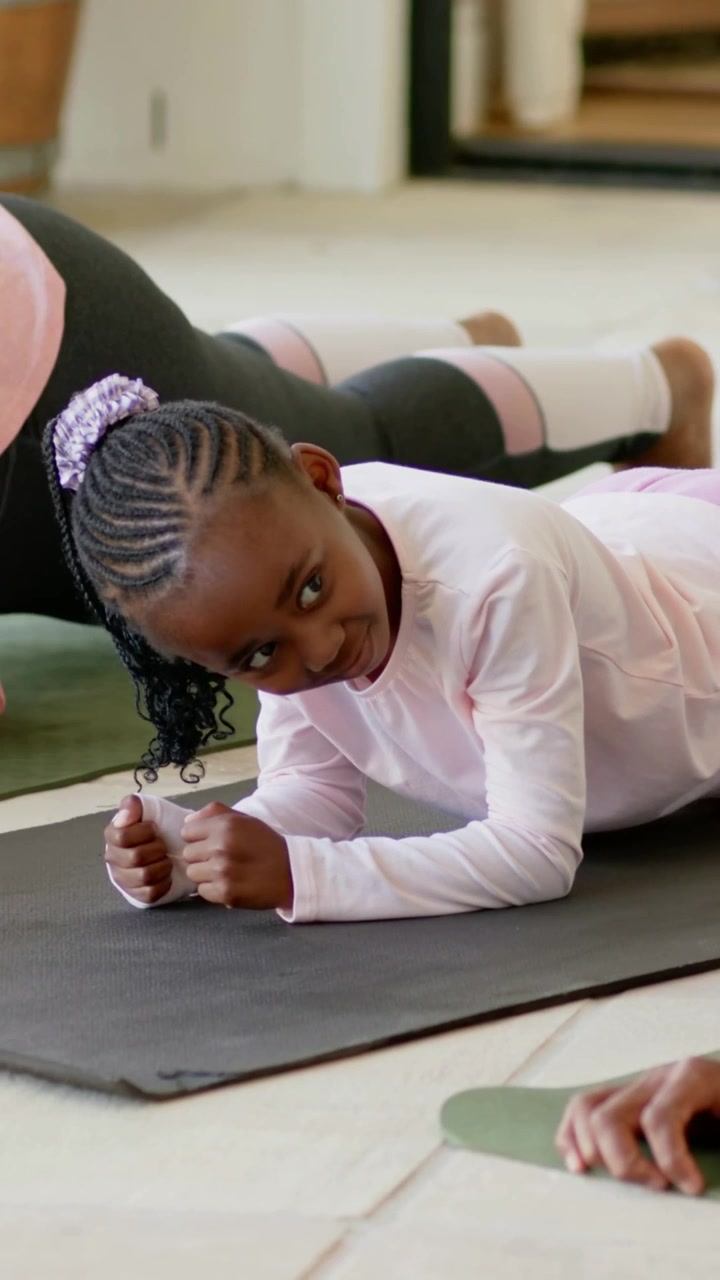 Vertical video: Kneeling, man guiding girl in pink into forearm plank for core at home with mats