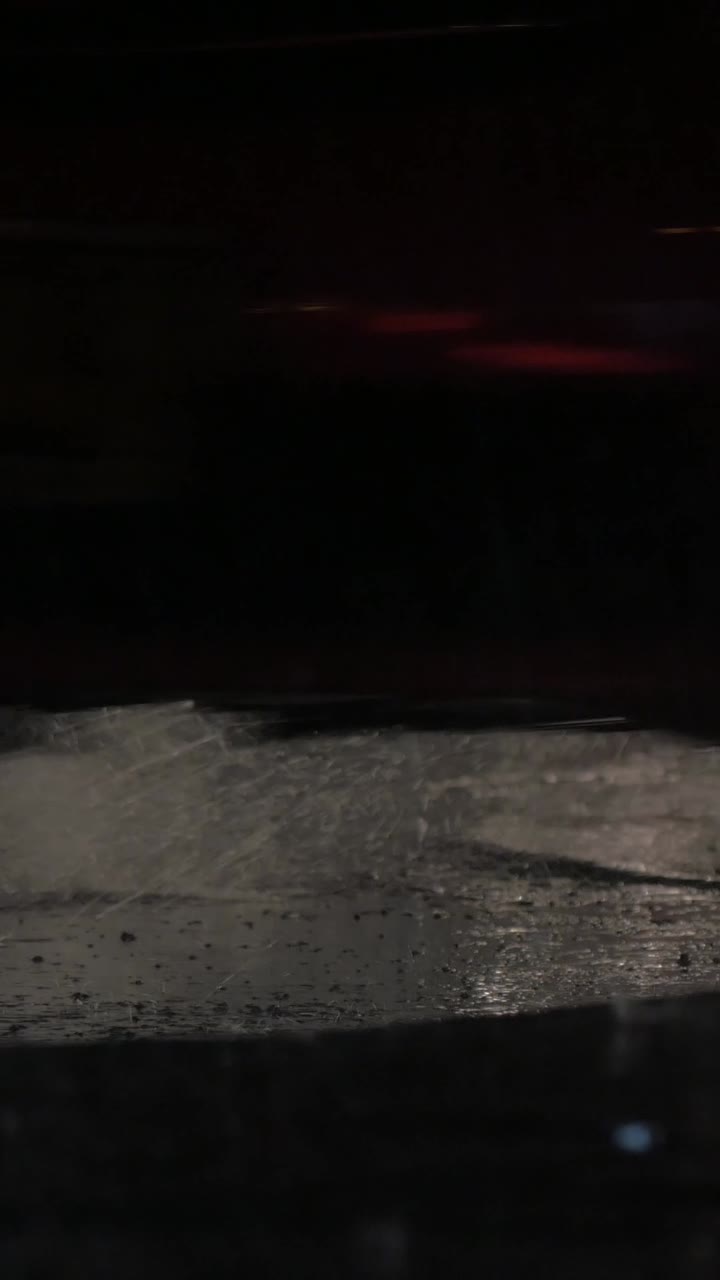 Ruote dell'auto che schizzano acqua su una strada notturna e piovosa.