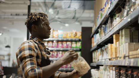 Worker-In-Apron-Arranging-Shelves-With-Products-At-Grocery-Shop,-Low-Angle-View