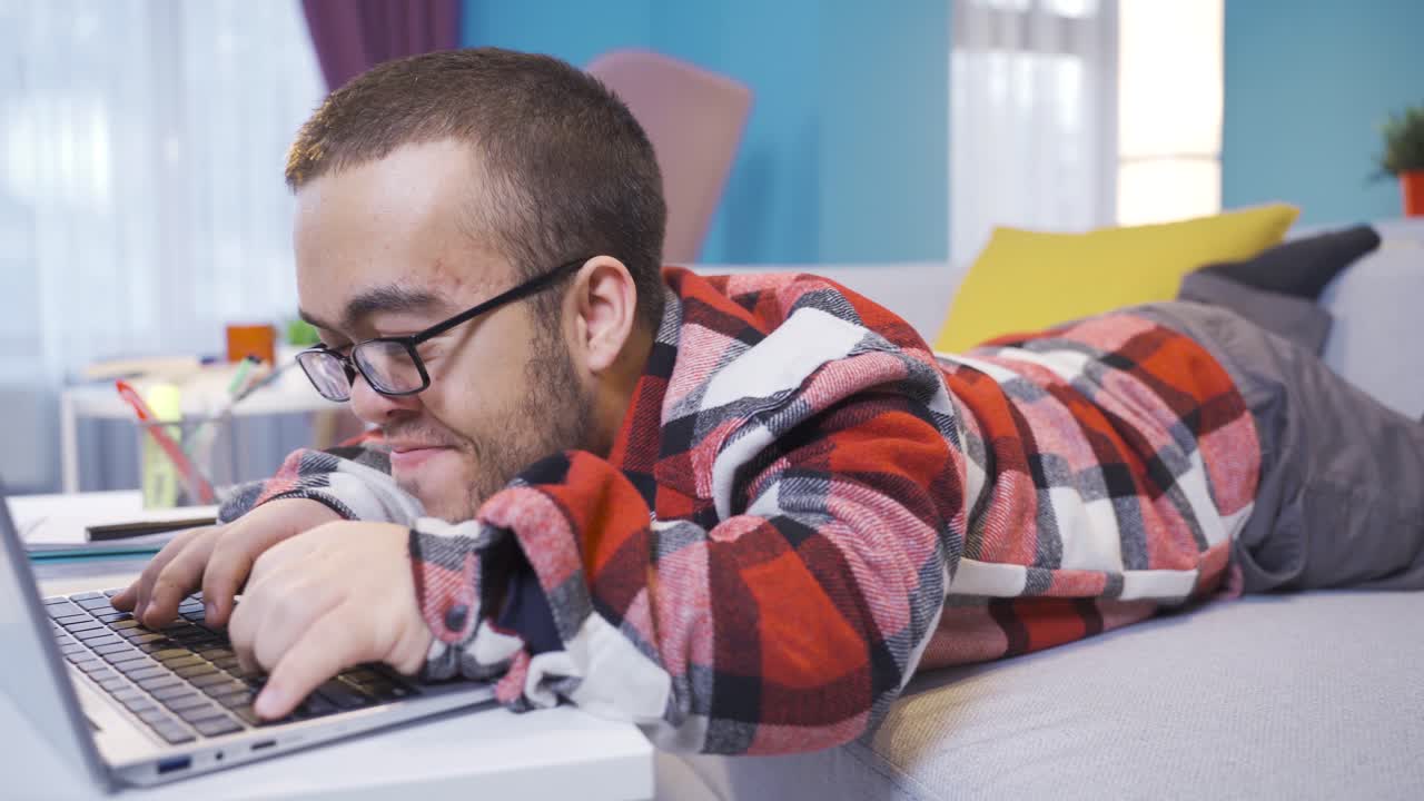 Midget man lying on the sofa works at the computer.