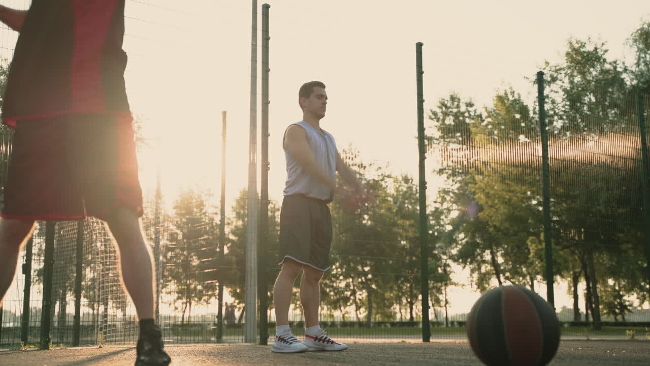 jugadores de baloncesto masculinos concentrados que se extienden en una cancha de baloncesto al aire libre al atardecer
