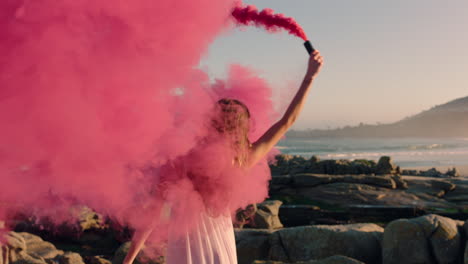 Hermosa-Mujer-Agitando-Granadas-De-Humo-Rosa-Bailando-En-La-Playa-Al-Amanecer-Celebrando-La-Libertad-Creativa-Con-Un-Movimiento-De-Baile-Juguetón