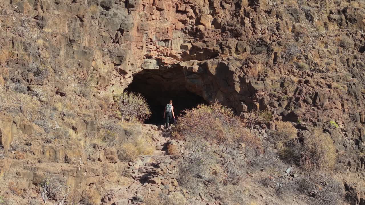 Ansite Fortress: Aerial view over Female hiker walking on a path towards a cave entrance in the mountains of Gran Canaria