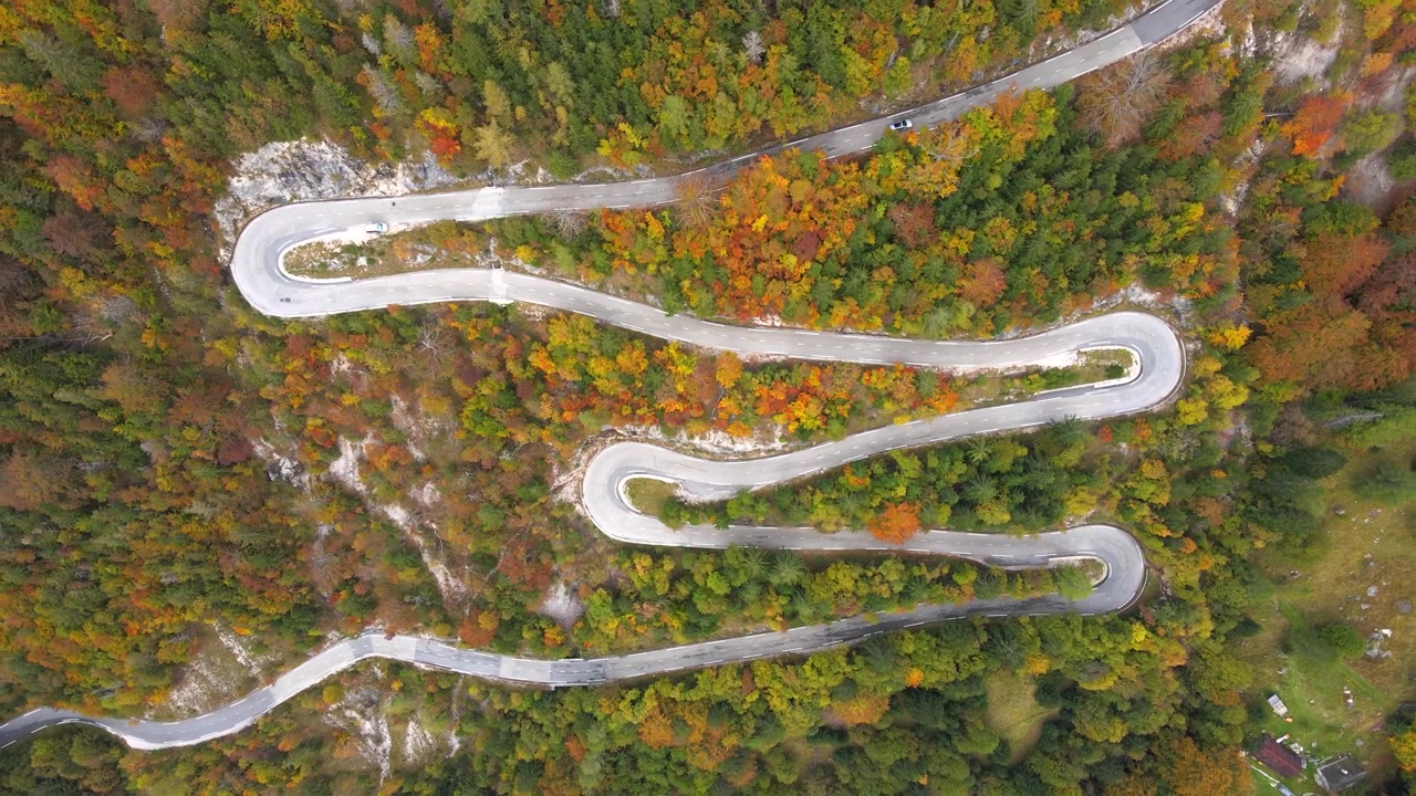 Directly overhead view of a car driving along the winding mountain road at Vršič Pass surrounded by lush forest, Slovenia