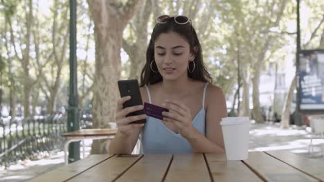 mujer joven que realiza el pago con tarjeta de plástico a través de un teléfono inteligente