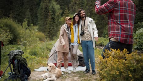 a guy in a red plaid shirt photographs a guy and two girls tourists in special hiking clothes against the backdrop of a green forest