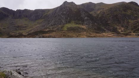 Panning-over-Llyn-Idwal,-beautiful-lake-in-Snowdonia-National-Park,-North-Wales-on-a-windy-day