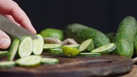 las manos de los hombres cortan el pepino en rebanadas redondas en una tabla de cortar de madera.