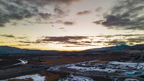 Aerial-hyperlapse-at-sunset-with-clouds-crossing-the-sky-over-the-mountains-and-cars-driving-along-the-highway