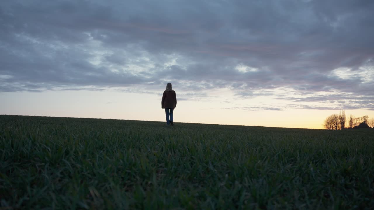Girl walking through a field of grass at sunset