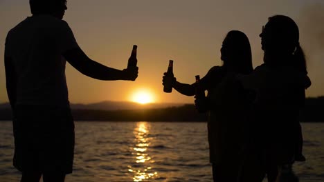 group of young latin friends toasting with beer bottles standing on a floating dock on a lake at sunset