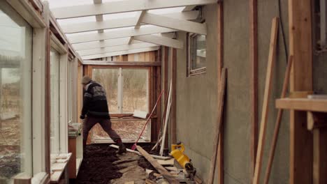 male worker walking inside greenhouse with unfinished interior to get wood material from outside