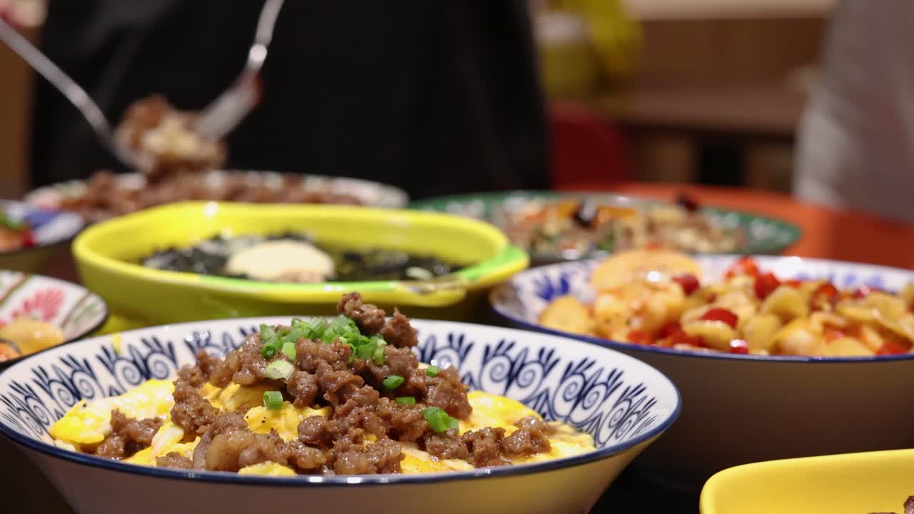 A person serves a traditional Thai egg, beef, and rice dish in a brightly lit indoor setting, with colorful plates and close-up camera movement