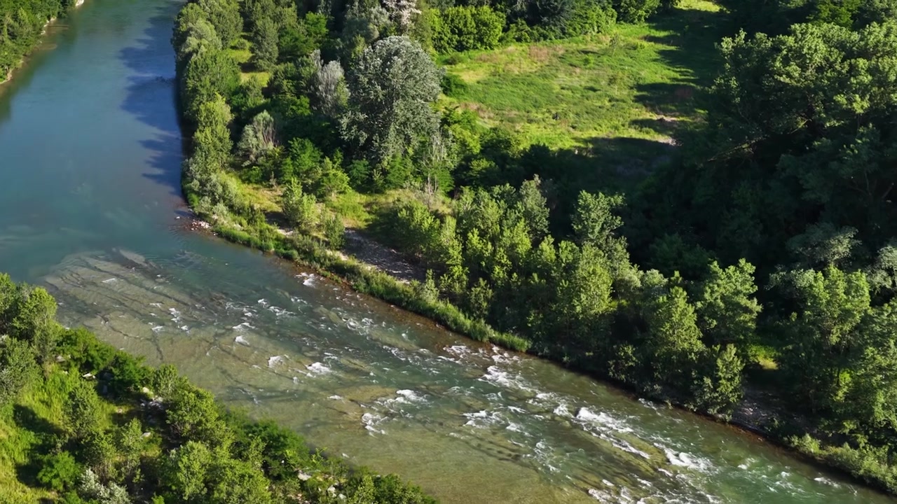 Ripresa con drone dall'alto cattura un fiume serpeggiante che scorre attraverso una foresta verde lussureggiante e prati.