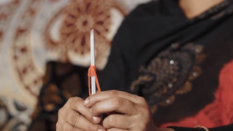 mujer india tejiendo la primera fila con hilo rojo y dos manualidades con agujas.