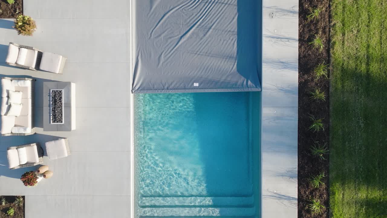 Overhead views of a modern backyard pool with cover mid-retraction and neat landscaping