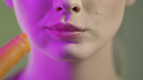 close-up of woman's mouth crunching and eating raw carrot, studio shot with colorful lighting