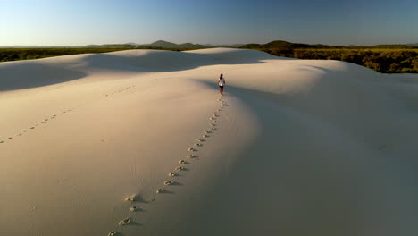 drone shot slow rising of man walking alone on sand dunes