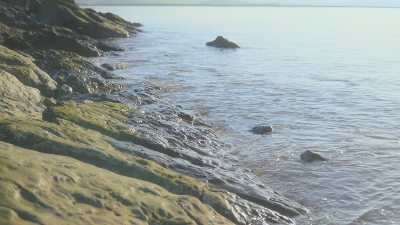Havet slår blidt mod glatte klipper i tidlig morgen efterårssol med langsom panorering opad