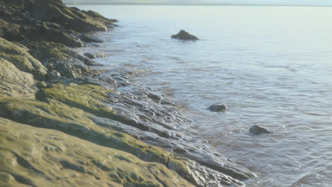 sea gently breaking against smooth rocks in early morning autumn sunlight with slow pan upwards