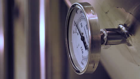 rack focus from a blurry view to a close-up of a temperature gauge mounted on a stainless steel fermentation tank in a brewery