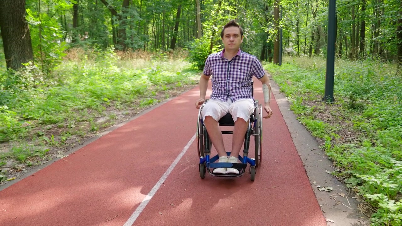 Young Man with Arm Cast Sits in Wheelchair on Park Path