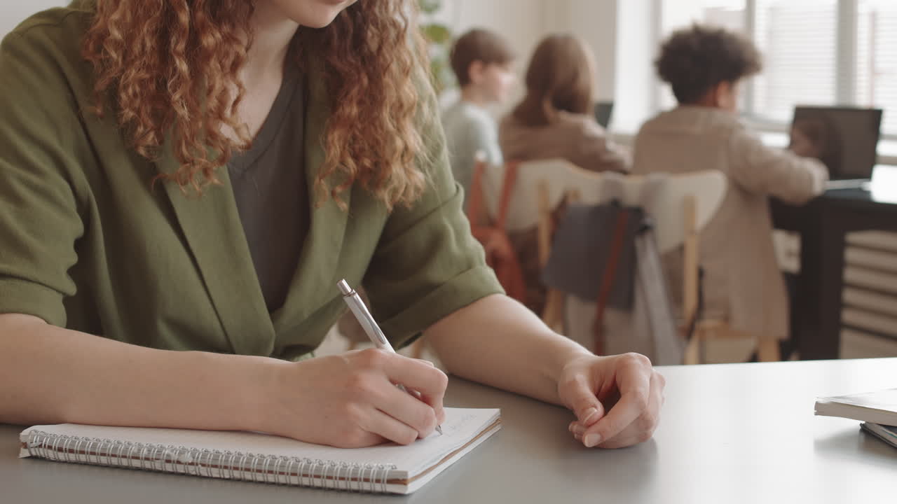 Woman Writing in Notebook in Classroom