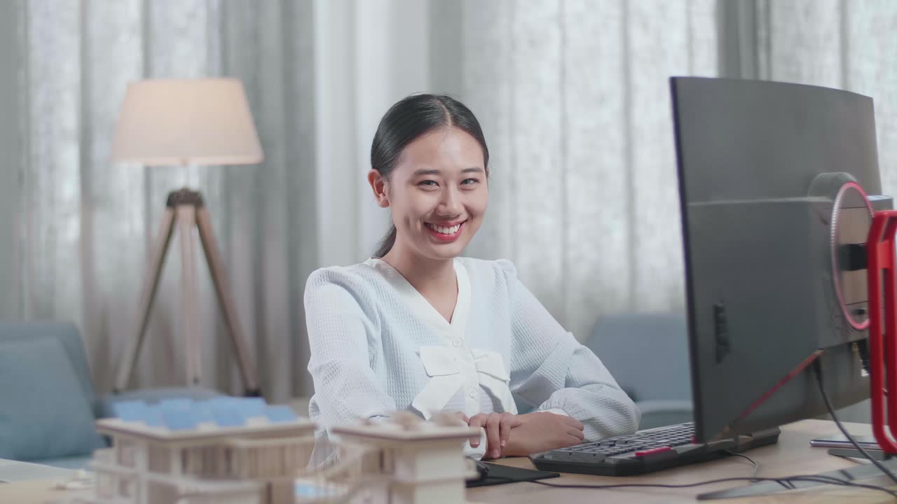 집에서 데스크에서 작업하는 동안 카메라에 미소 짓는 하우스 모델과 함께 아시아 여성 엔지니어
