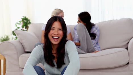 Una-Mujer-Sonriente-Se-Sentó-En-El-Suelo-Con-Amigos-Charlando-Detrás