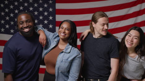 Studio-Portrait-Shot-Of-Multi-Cultural-Group-Of-Friends-Standing-In-Front-Of-American-Flag-Celebrating-4th-July-Independence-Day-1