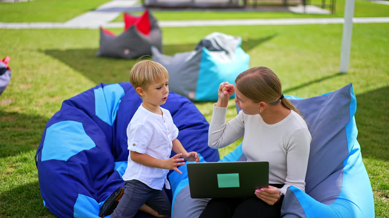 Woman and her son discussing video they watch on laptop. Family spending time outdoors in the garden in summer time. Blurred backdrop.