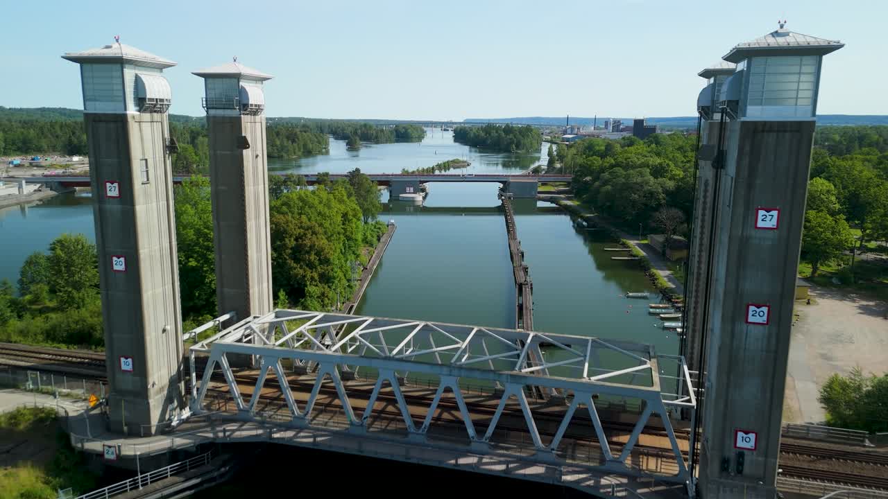 Drone lentää historiallisen metalliristikkorautatiesillan ohi Göta Älv -joen yli, paljastaen uuden Stridsbergsbron-sillan ja urbaanin kaupunkisilhuetin aurinkoisena kesäaamuna Ruotsissa