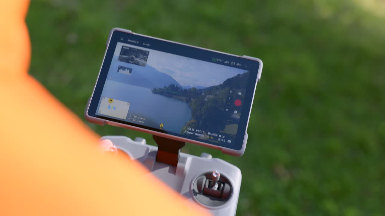 A drone pilot is using a remote control with a screen displaying an aerial view of a landscape The operator is controlling an unmanned aircraft system for photography and videography purposes