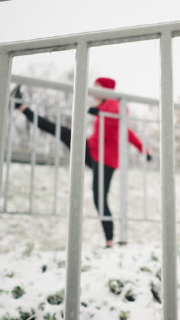 close up iron rail covered with snow frost snowy ground blurry background woman working out stretching leg back and forth surrounded by frost covered trees in foggy winter atmosphere