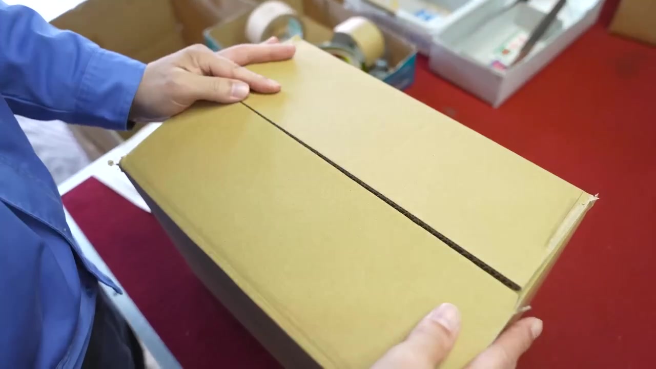 Worker closing large cardboard shipping box packed with cutlery ready for delivery