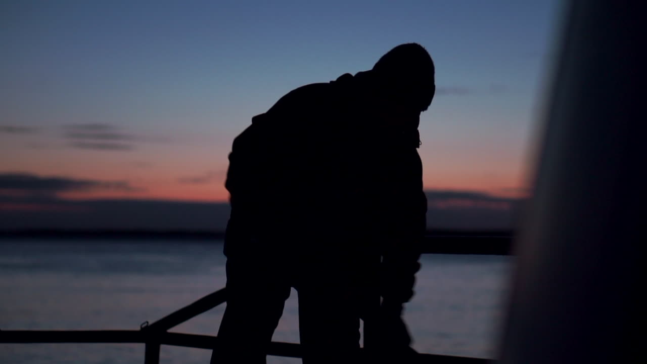Silhouette of a person working on a boat at dusk