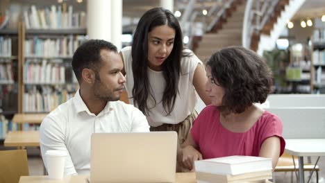 Serious-students-sitting-at-table-in-library-with-laptop