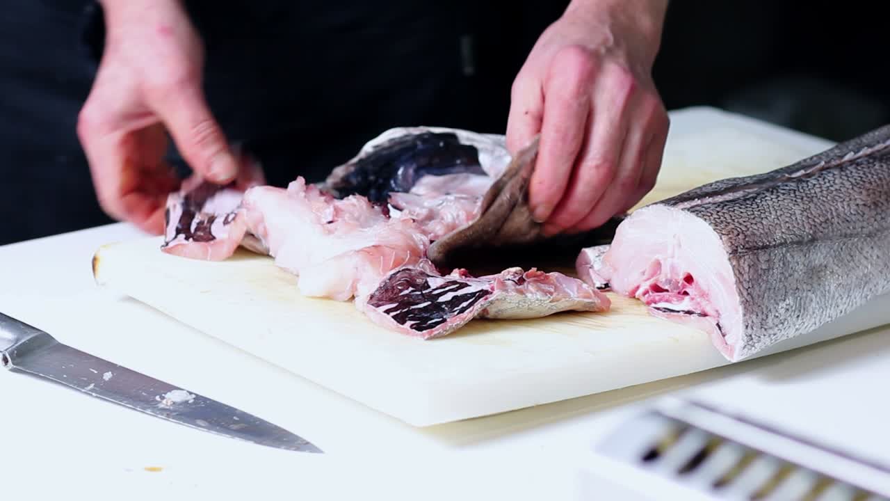 Cook hands cleaning hake's head over a cutting board in a Spanish restaurant