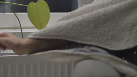 person in blanket freezes, reaches for heater to check temperature