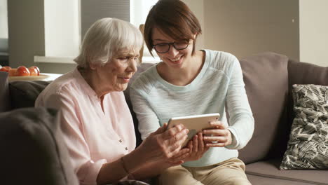 caring female volunteer showing retired woman how to use tablet computer application