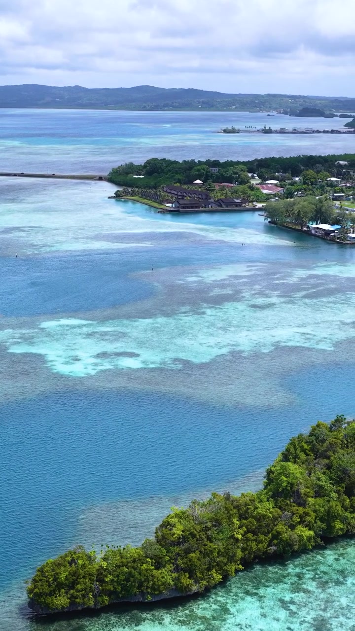 Una ripresa aerea con drone effettua una panoramica su acque turchesi, isole verdi lussureggianti ed edifici di resort costieri.