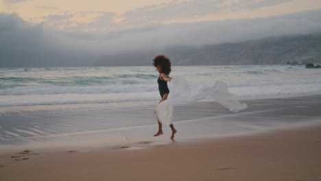 girl running beach pareo swaying on summer wind. woman jogging with satin fabric