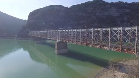 Beatifully-aged-old-baltimore-type-metal-bridge-with-stone-pilars-and-rusty-look-on-lake,-aerial