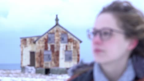 young girl looks at camera while focus switches from a rusty house in the background to her face. stable closeup macro shot on 90mm