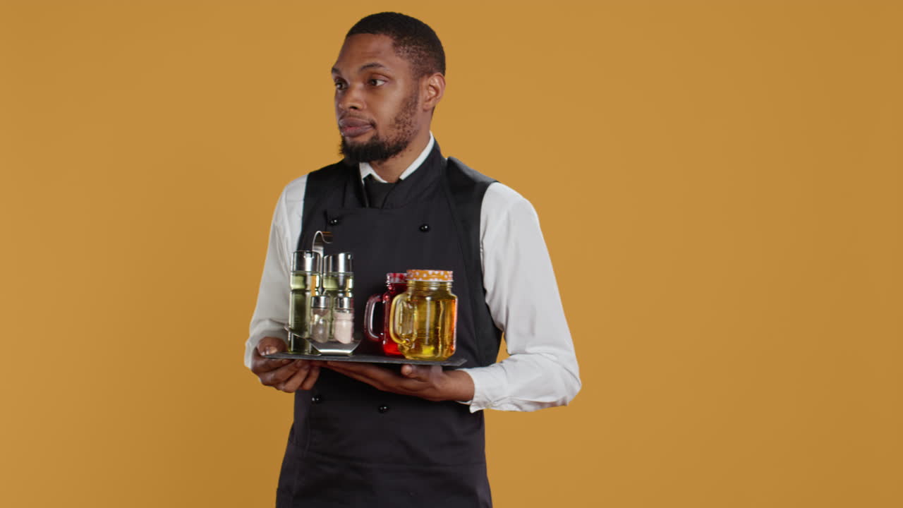 Waiter bringing drinks in glasses on a tray for clients at a table,